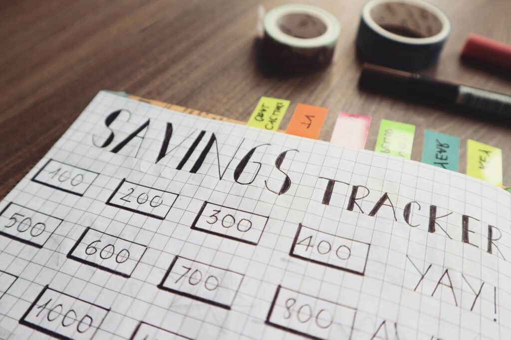 Graph paper with "Savings Tracker" written in pencil at the top and rectangles in rows and columns across the page with savings goals in them.