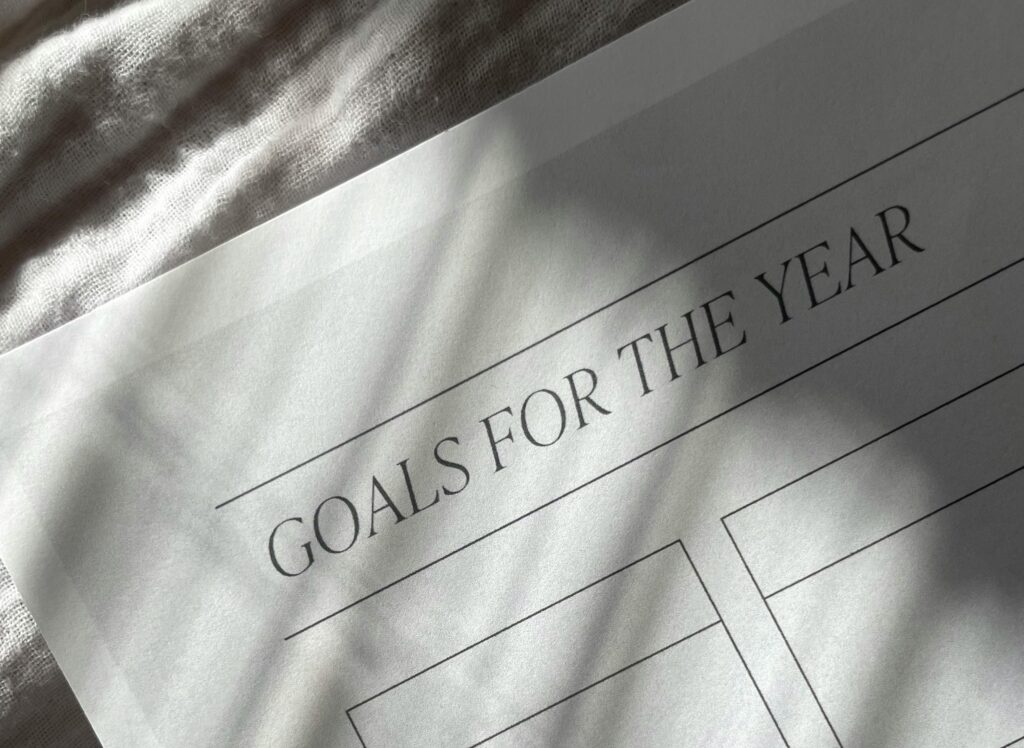 A sheet of paper title Goals for the Year with blank boxes to fill in your goals laid on a grey tablecloth