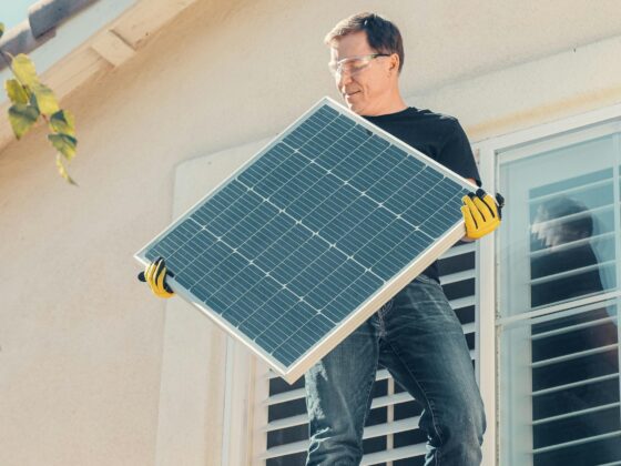 Photo of a man on a tile roof holding a solar panel to install solar energy on his home.