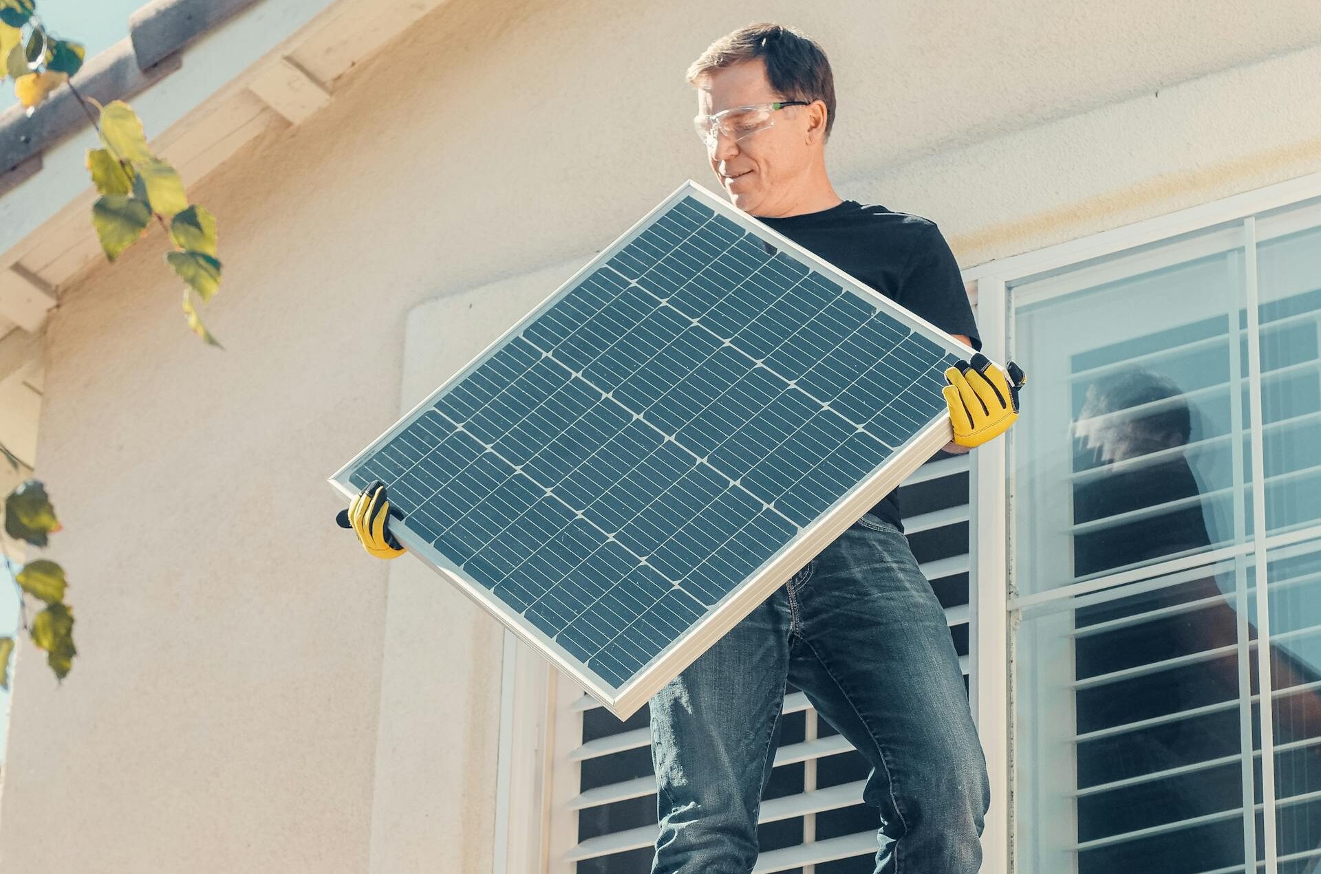 Photo of a man on a tile roof holding a solar panel to install solar energy on his home.