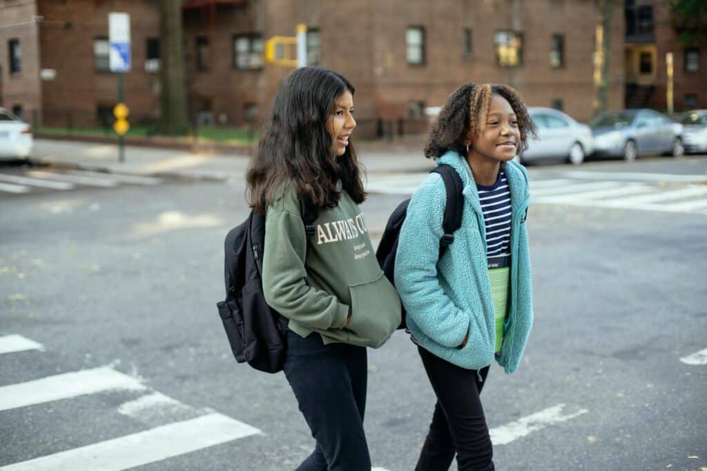 Two young girls with backpacks crossing the street on their way home from school.