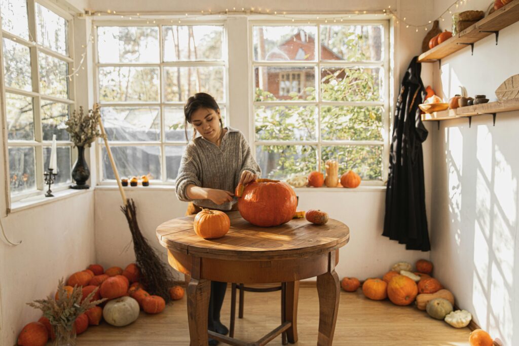 Woman carving pumpkins on a round wooden table in a room filled with windows and natural light