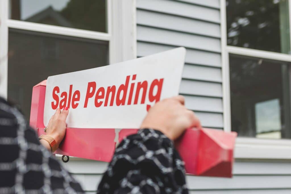 Sale Pending sign in front of a house with grey siding.