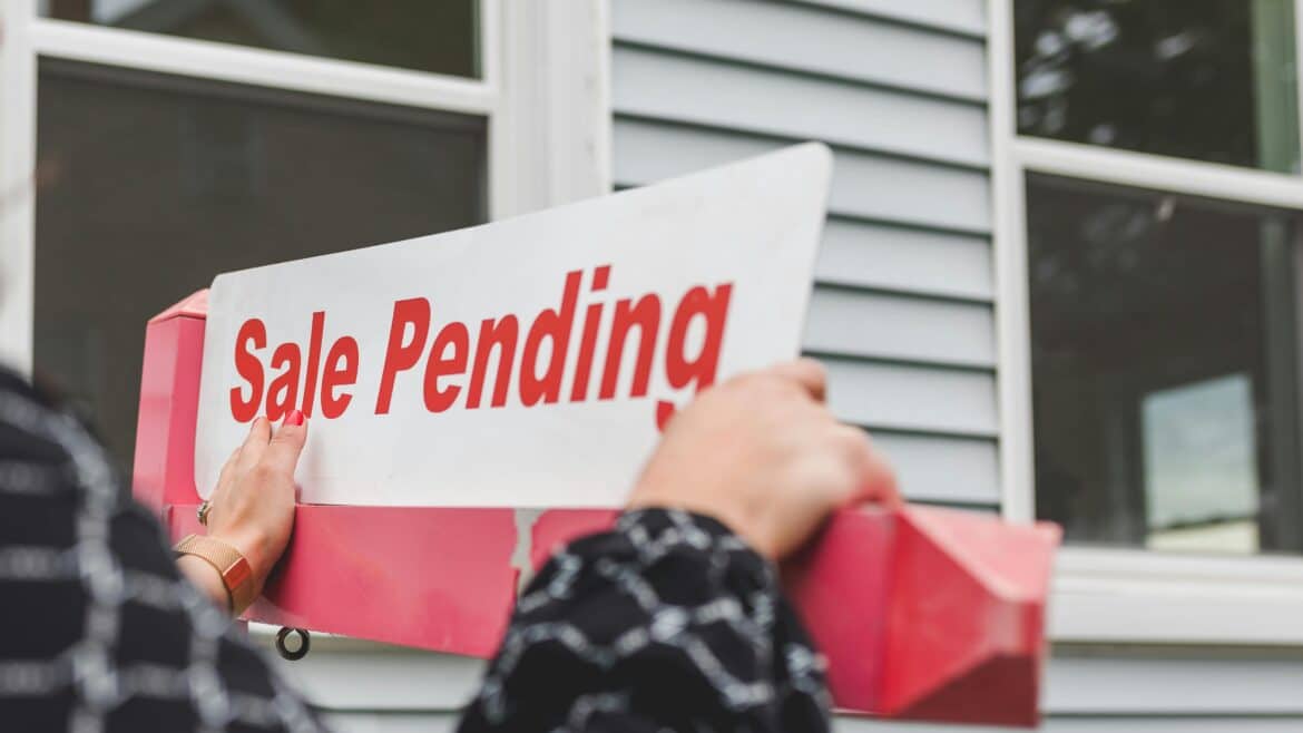 Sale Pending sign in front of a house with grey siding.
